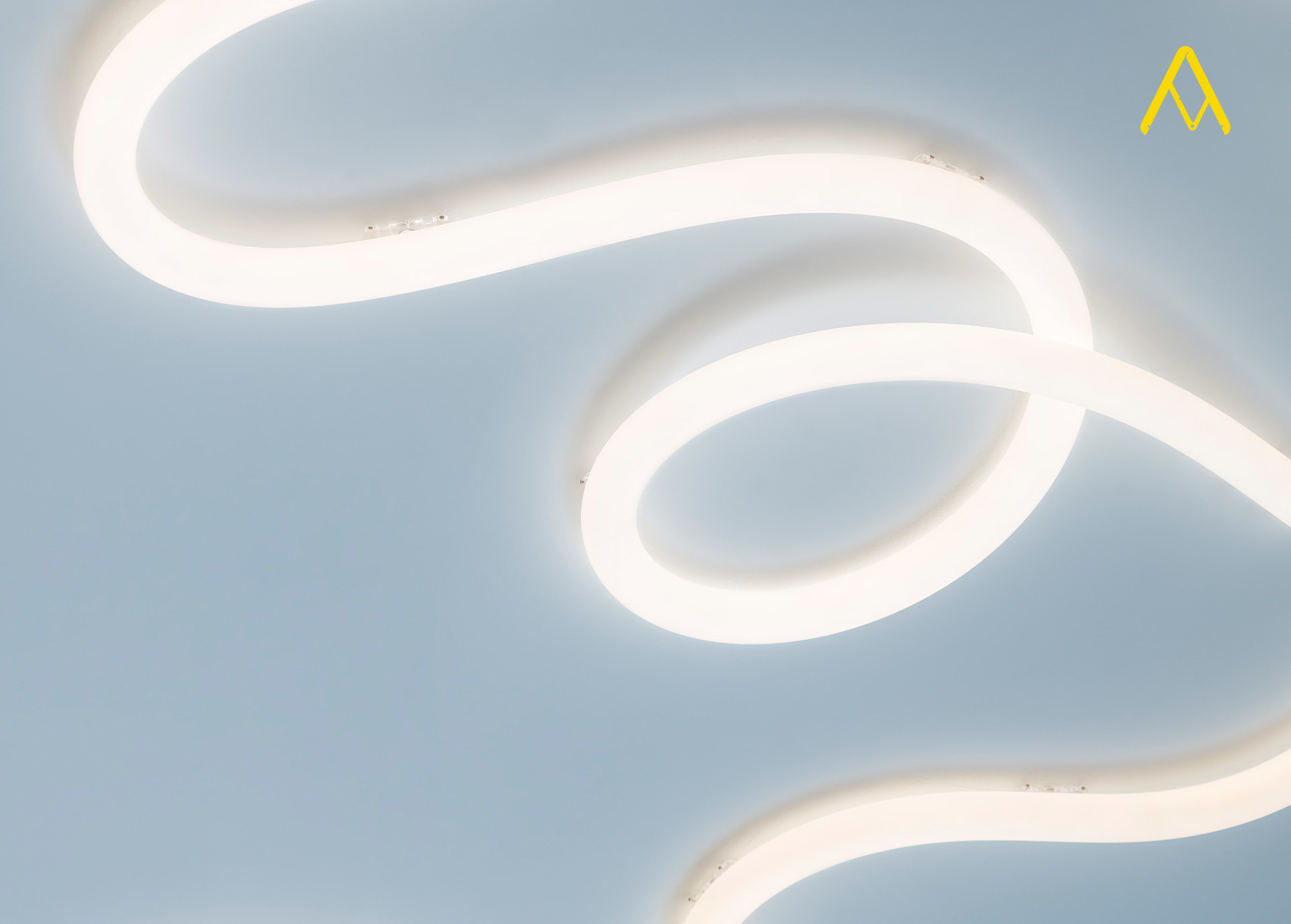 Artemide flexible LED light strip forming elegant curves and loops on a pale blue ceiling, emitting soft white light