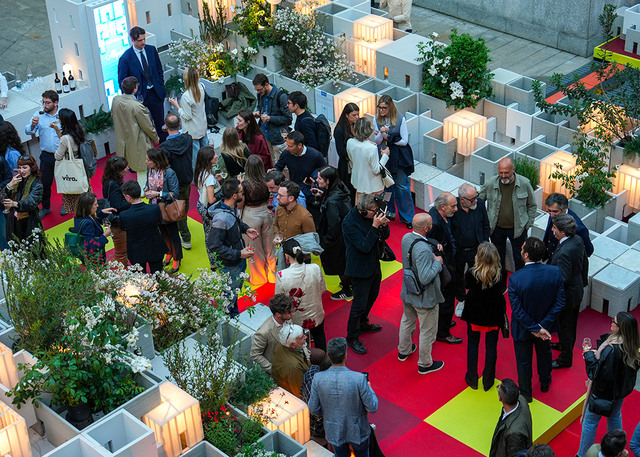 Overhead of a modular architectural installation with integrated greenery, red flooring and people within the exhibition space.