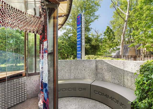 Rear view of the ticket booth with curved “Voice of Commons” bench and external totem.