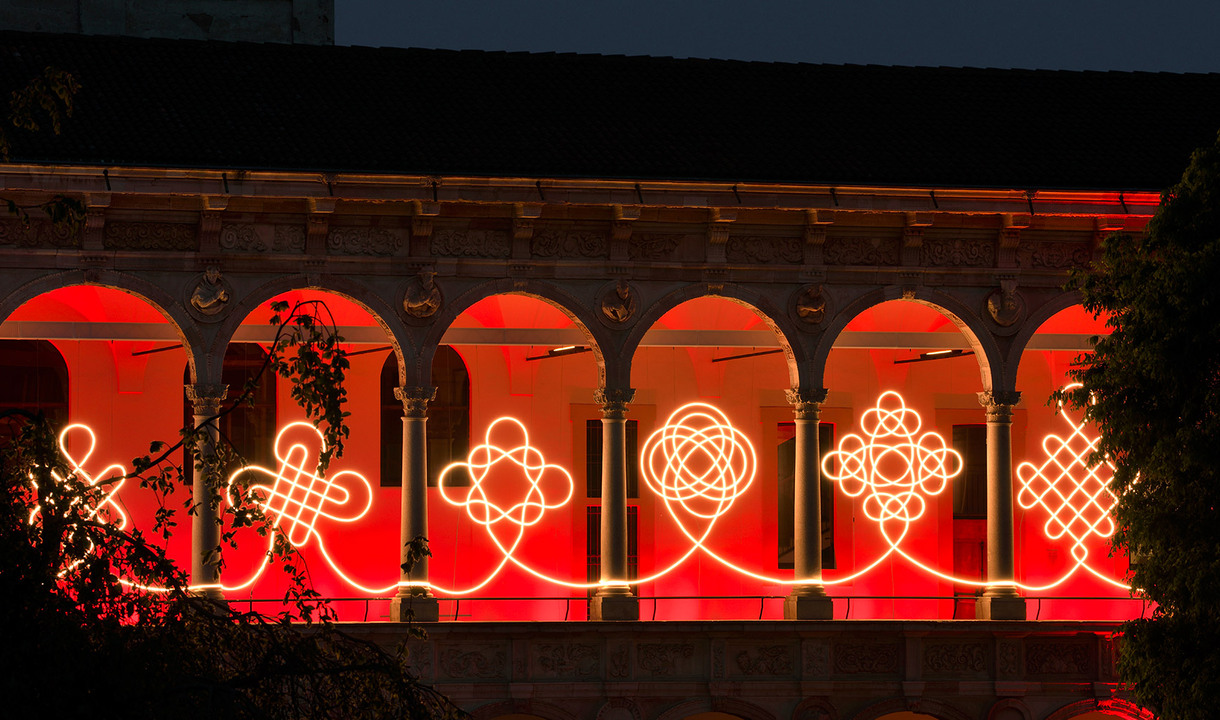 Front view of the portico of the University of Milan with a continuous light installation running across the arches.