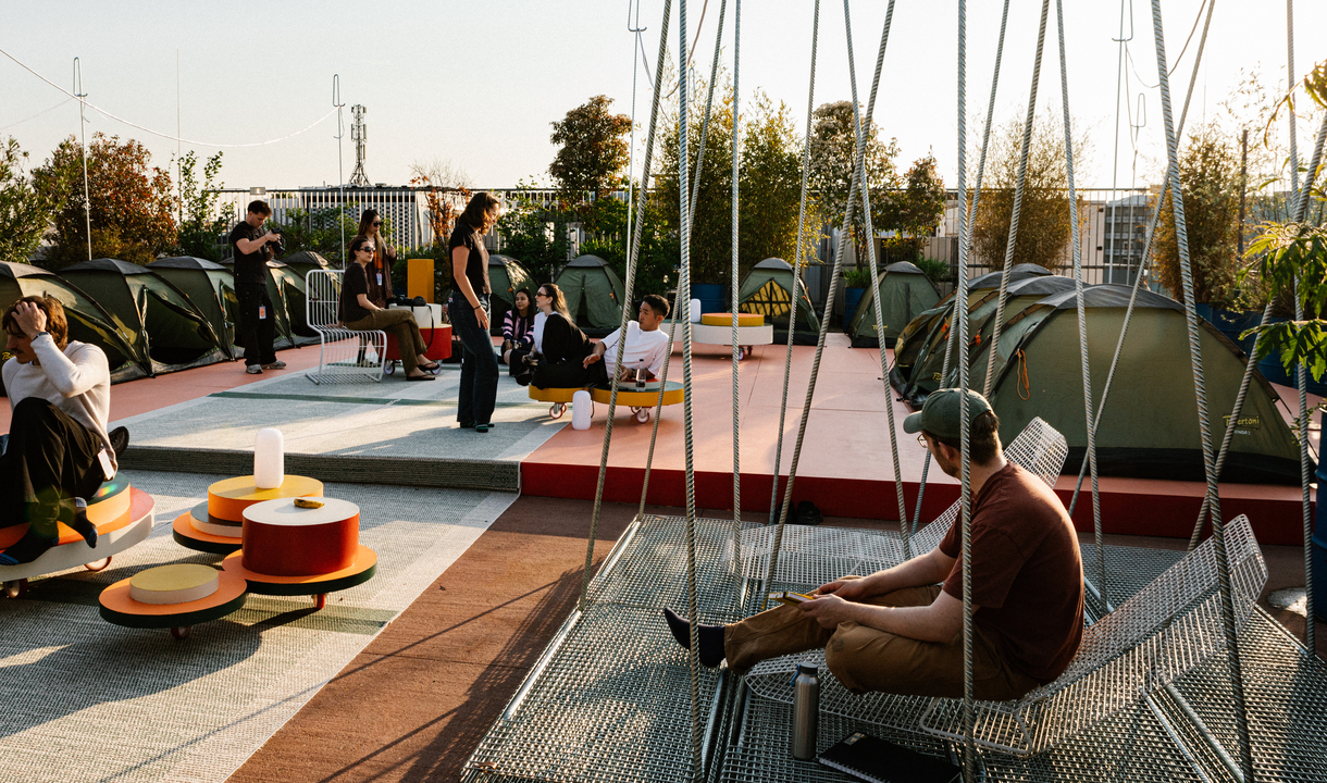 Outdoor installation with tents, suspended seating and colorful furniture on a terrace, animated by people at sunset.
