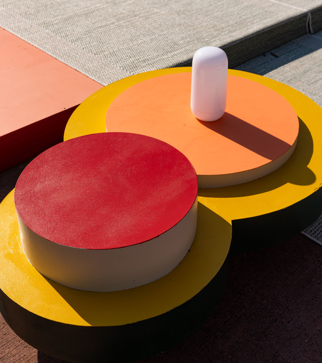 Detail of colorful circular tables with a white portable Gople lamp, photographed in an outdoor installation.