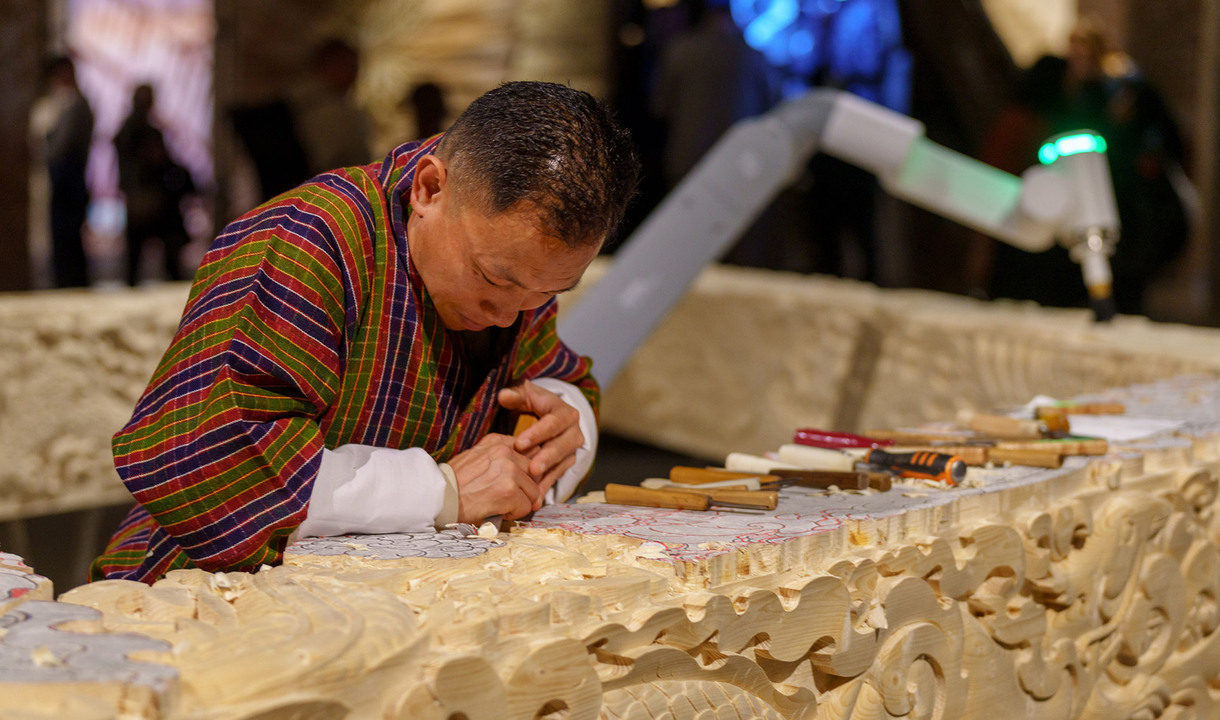 Bhutanese artist carves a wooden sculpture in collaboration with a robot.