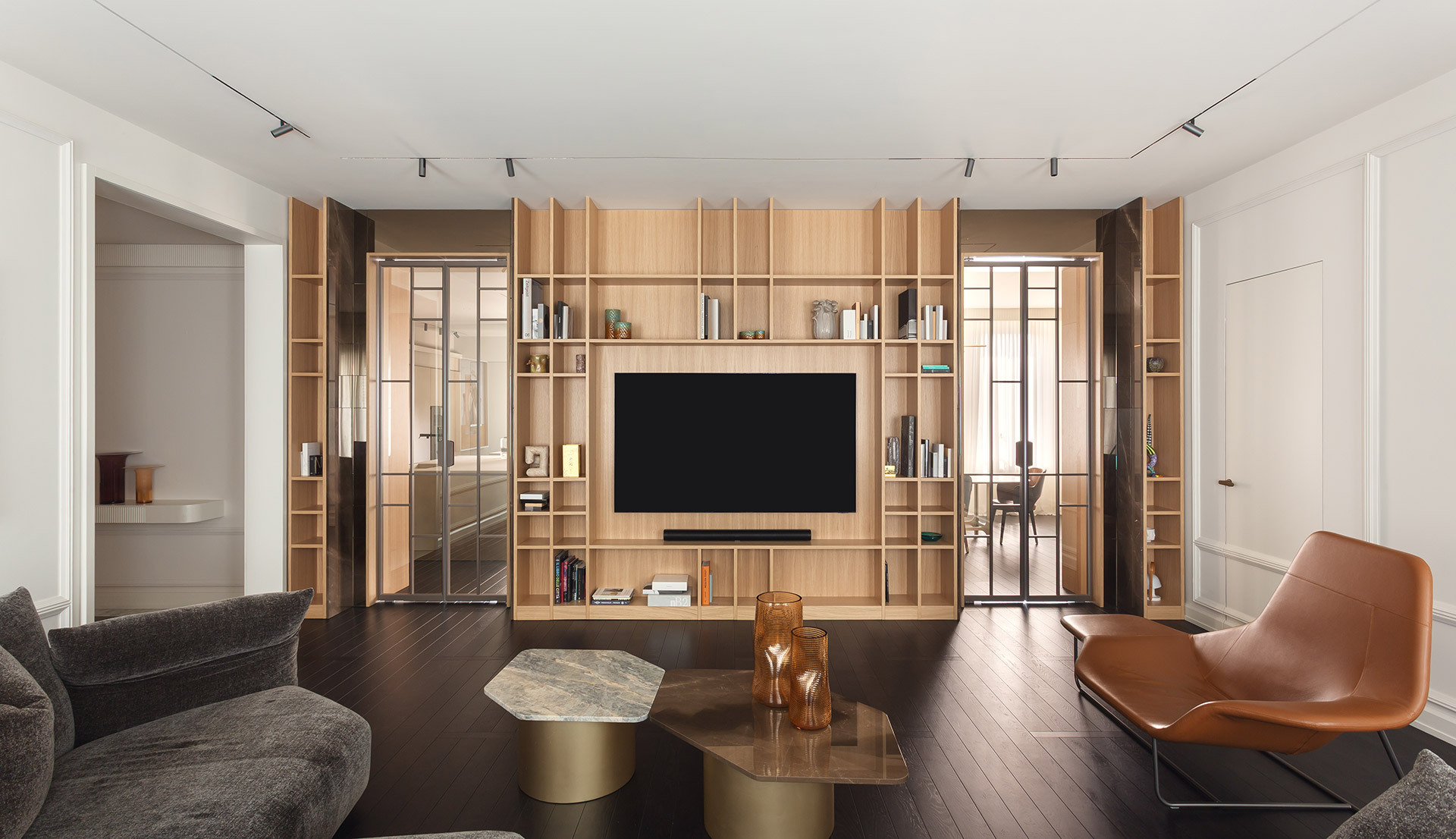 Living room with wooden bookcase, TV and ceiling track lighting.