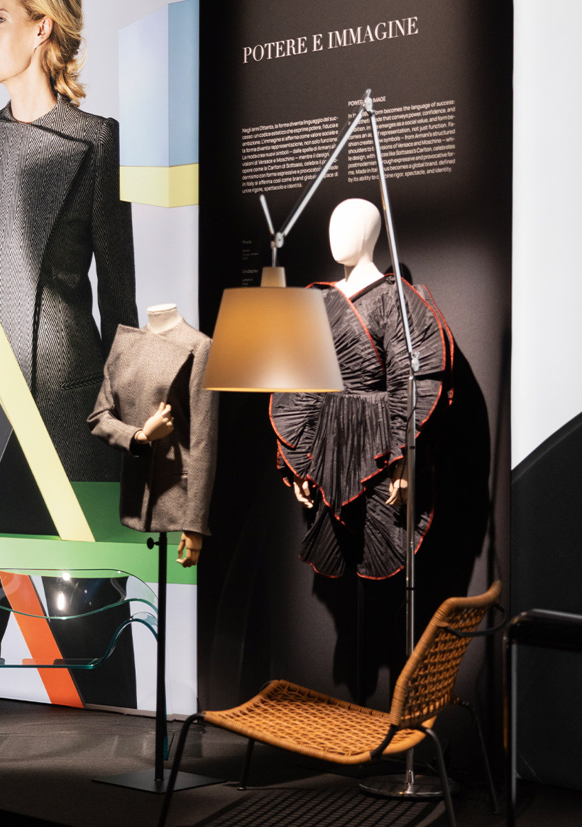 Lit Artemide Tolomeo Mega floor lamp displayed beside a mannequin wearing a dress and a wicker chair at the ABITO exhibition.
