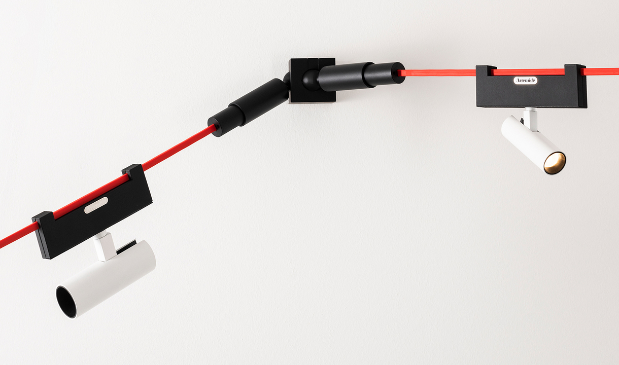 Artemide track lighting system with red cable, black connectors, and two white adjustable cylindrical spotlights mounted on ceiling