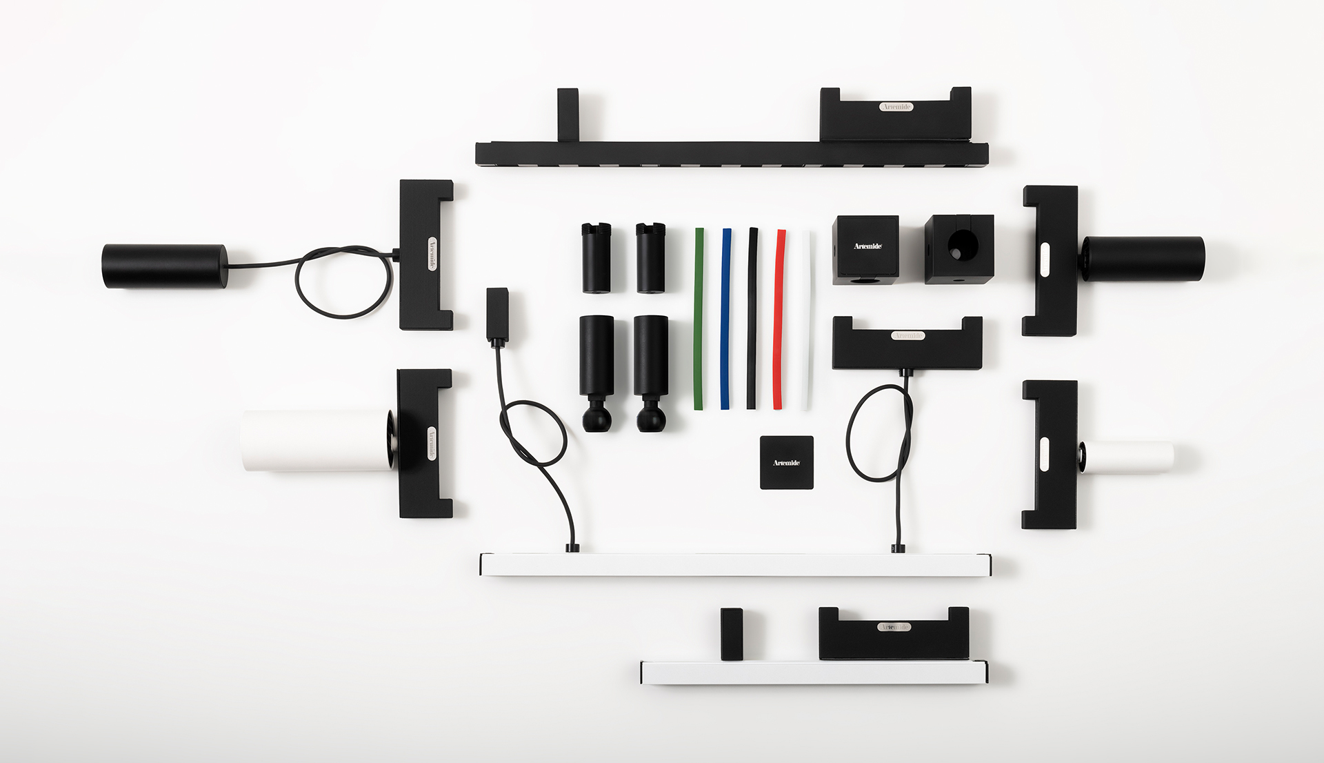 Artemide lighting system components laid flat: black and white modular parts, connectors, cables, and colored rods arranged on white background