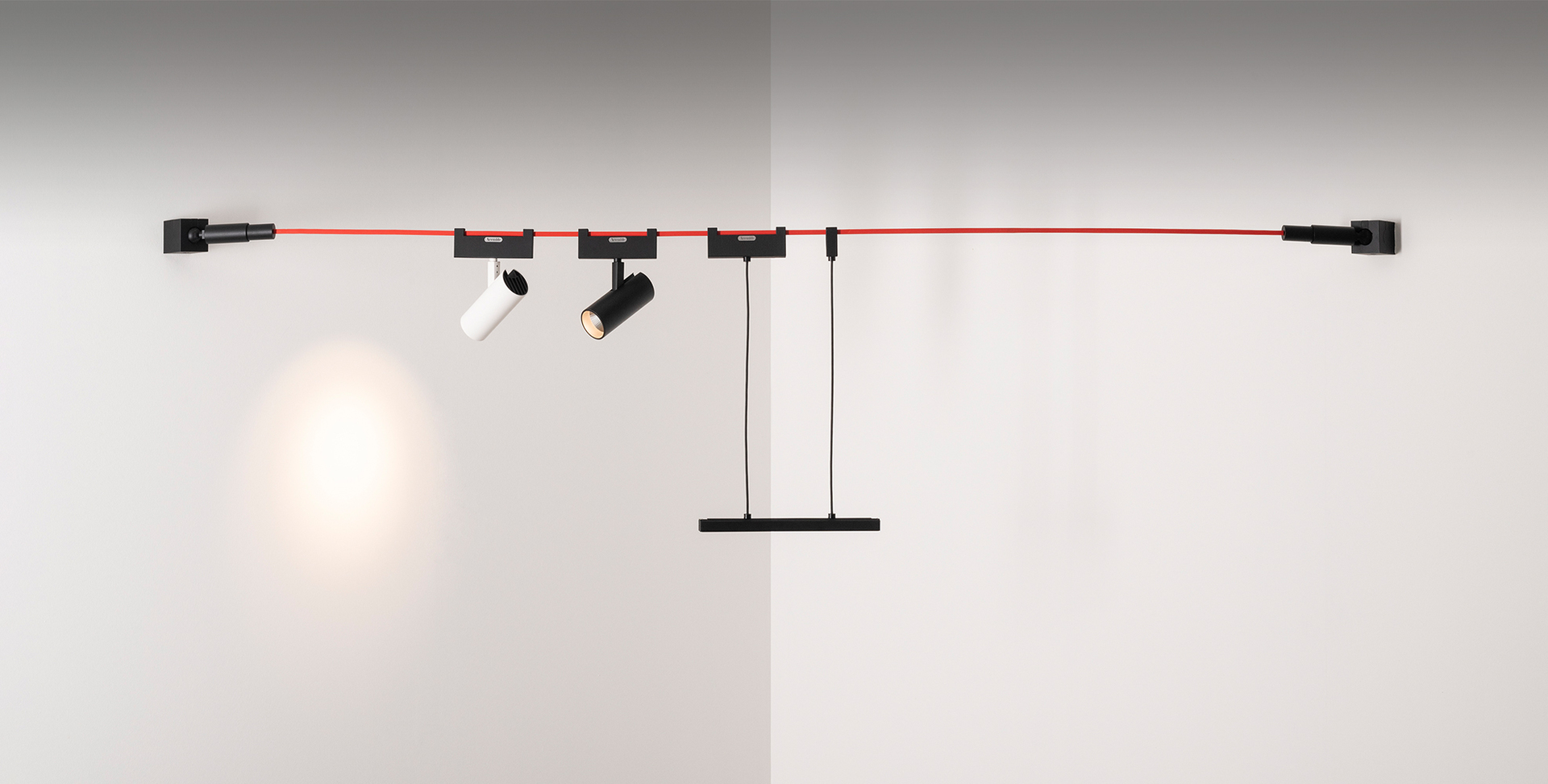 Artemide wall-mounted track system with red cable, two adjustable black spotlights, one white spotlight, and a pendant bar light.