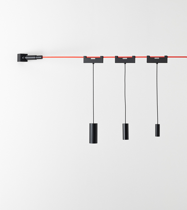Artemide wall-mounted track light system: red horizontal rail with three black pendant cylinder spotlights on adjustable black cables