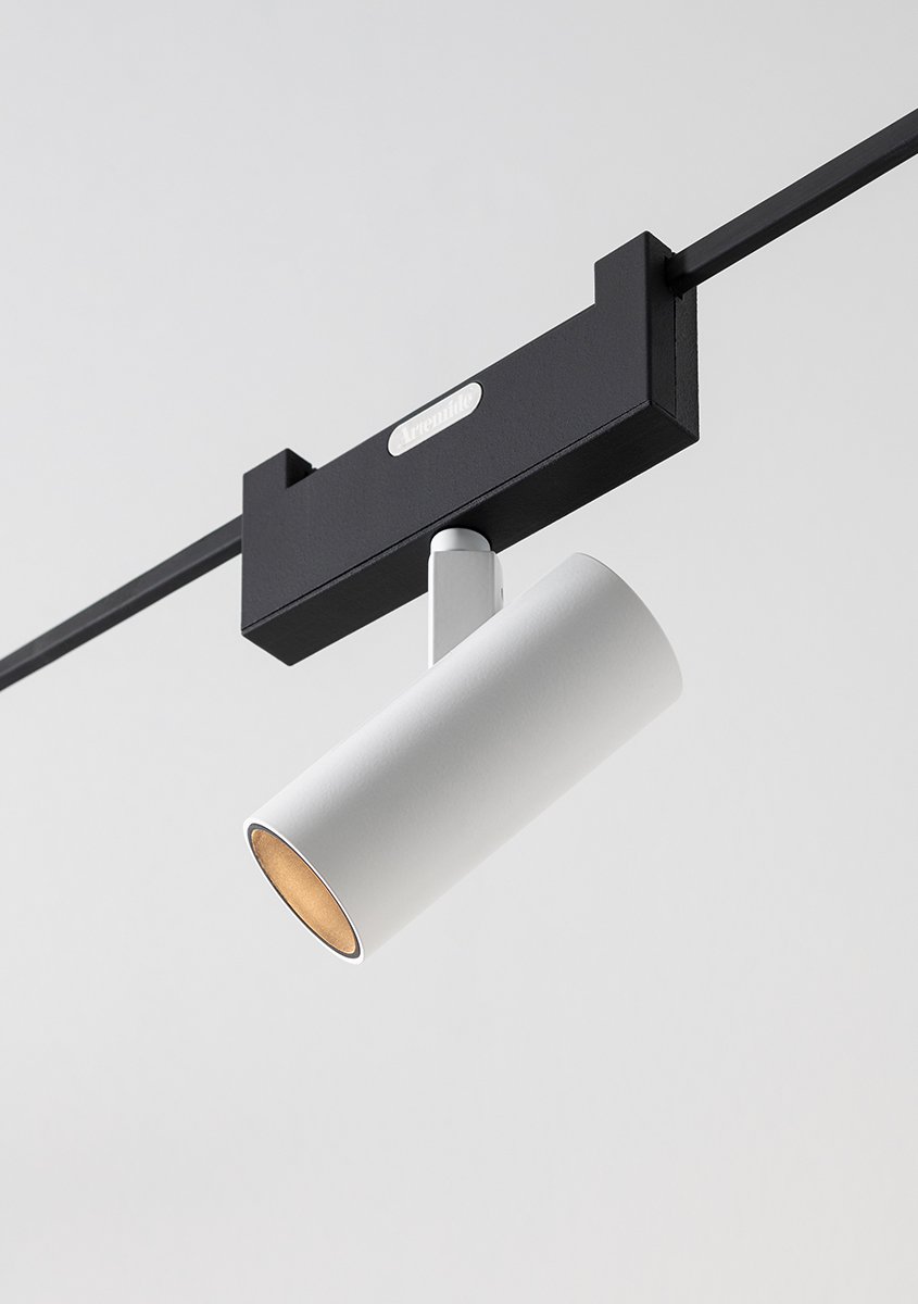 White cylindrical track spotlight mounted on a black rail, angled downward, with warm gold interior reflector.