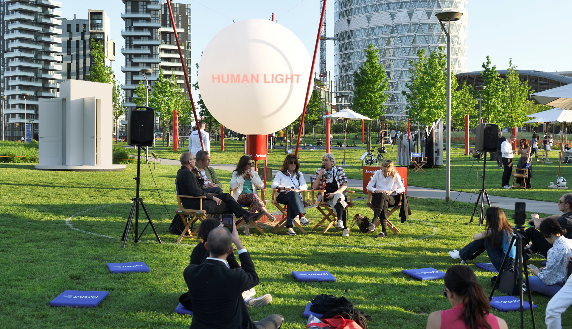 Outdoor panel discussion at Artemide 'Human Light' event, speakers seated in chairs on grass with a large illuminated white balloon