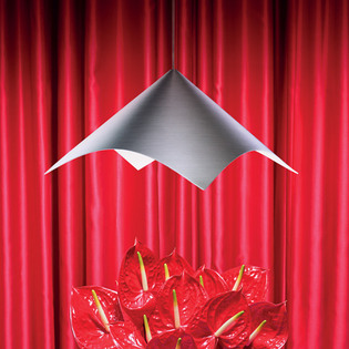 Iperbole metal pendant lamp above a cluster of red anthuriums, set against a backdrop of red curtains. Photo by Pierpaolo Ferrari.