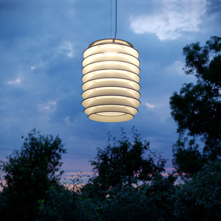 Slicing pendant lamp glowing in an outdoor landscape at dusk, with trees silhouetted in the background.
