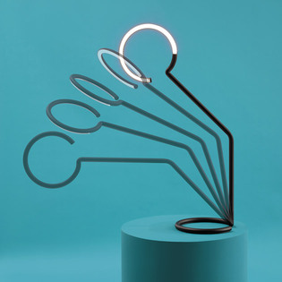 Vine Light lamp with multiple curved profiles fanned out on a blue pedestal, with one illuminated element at the top. Photo by Pierpaolo Ferrari.