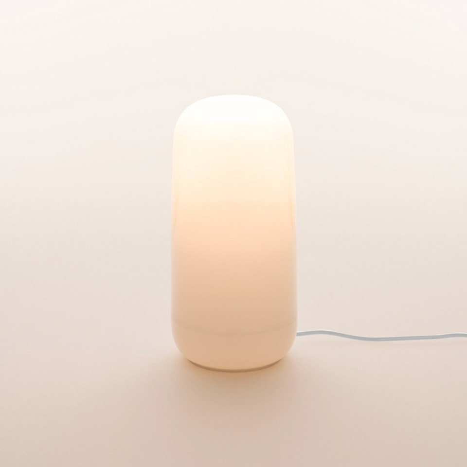 Artemide Gople Portable table lamp: luminous white opal glass capsule-shaped diffuser emitting warm ambient light, with white cable