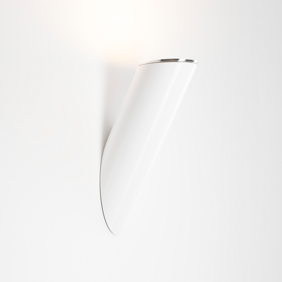 Artemide Ilio wall lamp, white conical shade angled upward with chrome rim, casting indirect light on the wall
