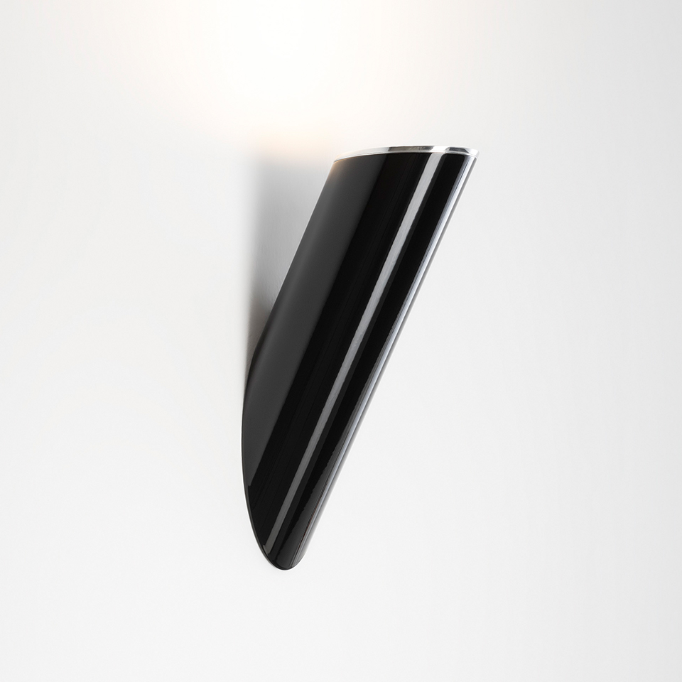Artemide Ilio wall lamp, glossy black elongated curved body, directing warm light upward against a white wall