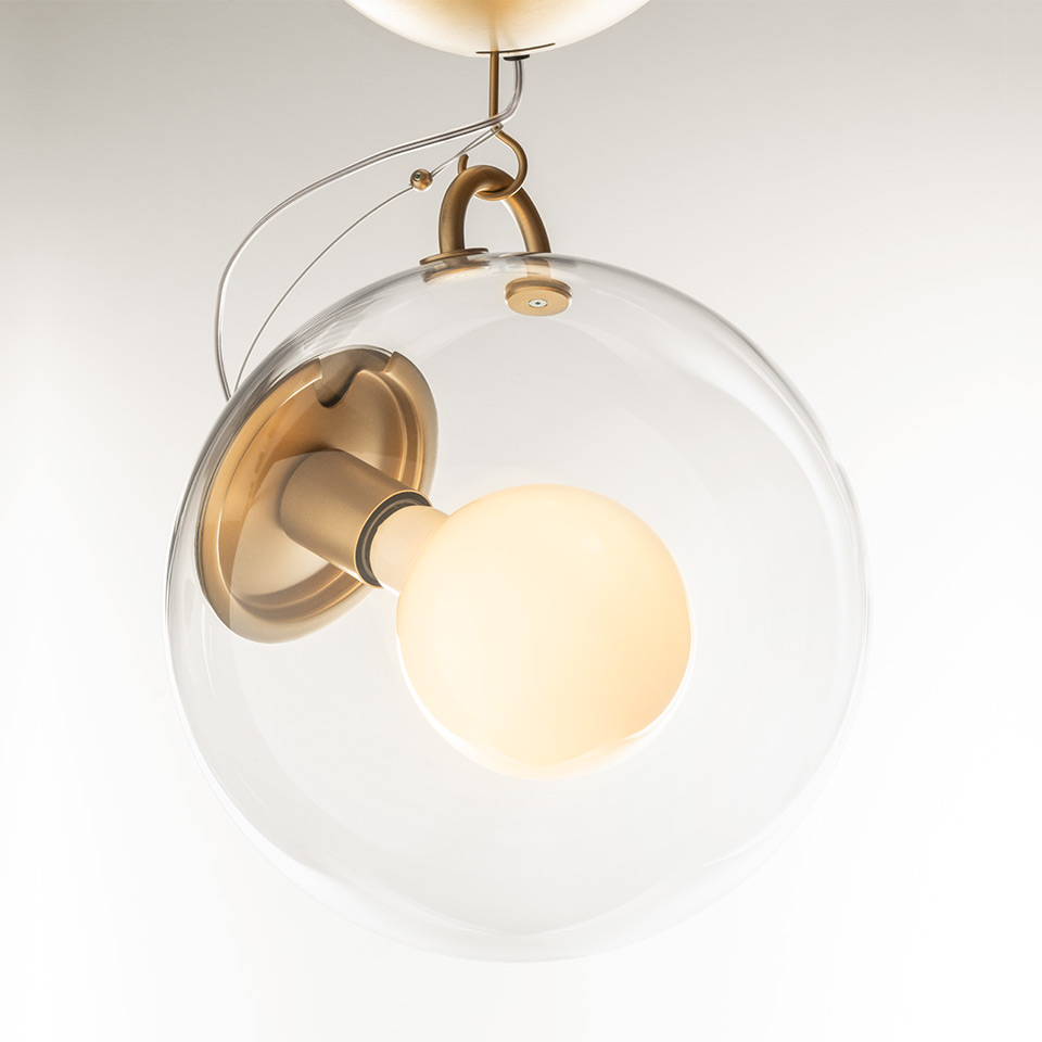 Artemide Miconos pendant lamp: clear spherical glass globe enclosing a frosted bulb, with antique brass metal hardware and suspension wire