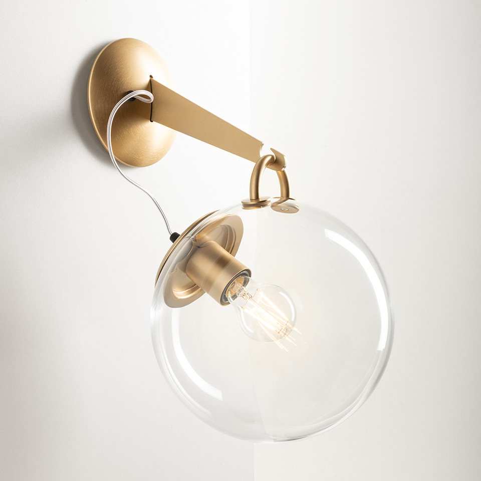 Artemide Miconos wall lamp: brushed gold arm and canopy holding a clear glass globe shade with vintage Edison bulb