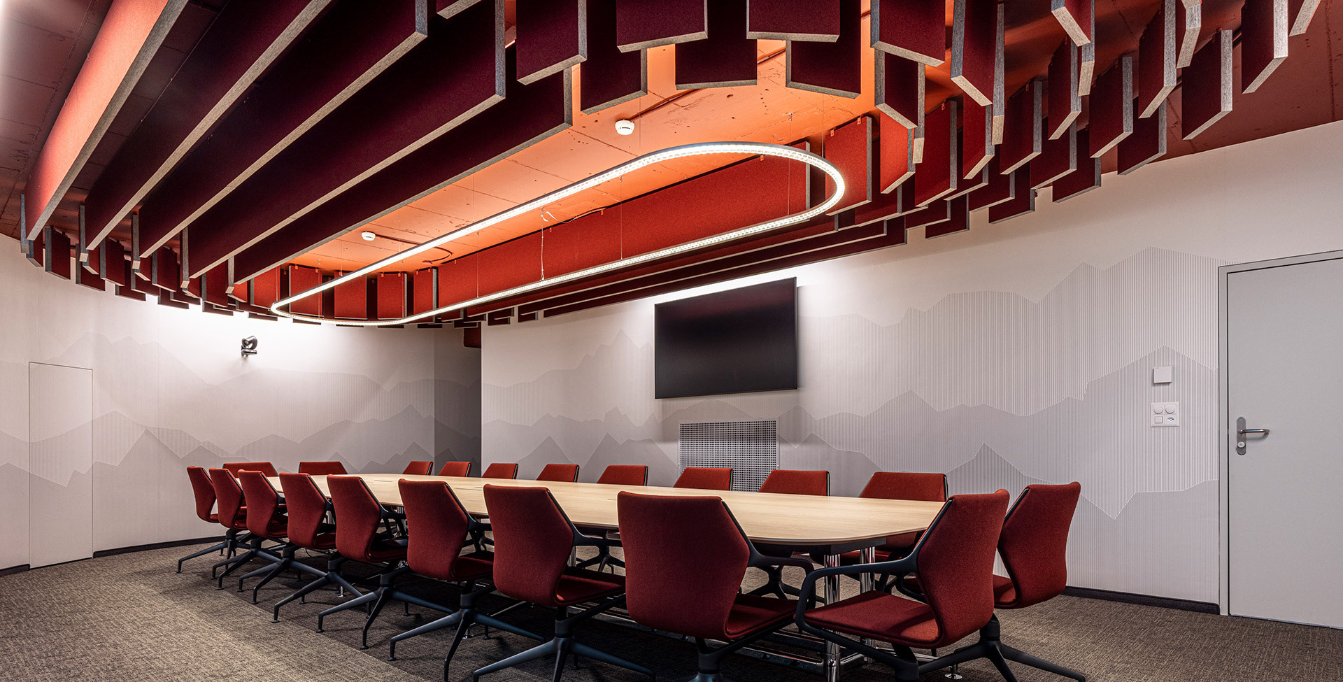 Suspended Somnĭum System light fixture above the table in a meeting room with acoustic ceiling panels.