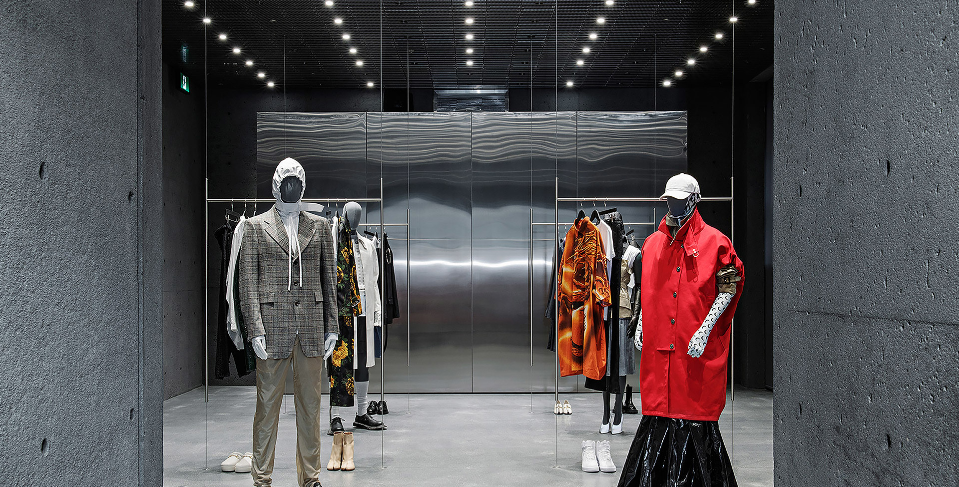 Fashion retail interior with Artemide recessed spotlights illuminating mannequins dressed in designer clothing against metallic wall panels.