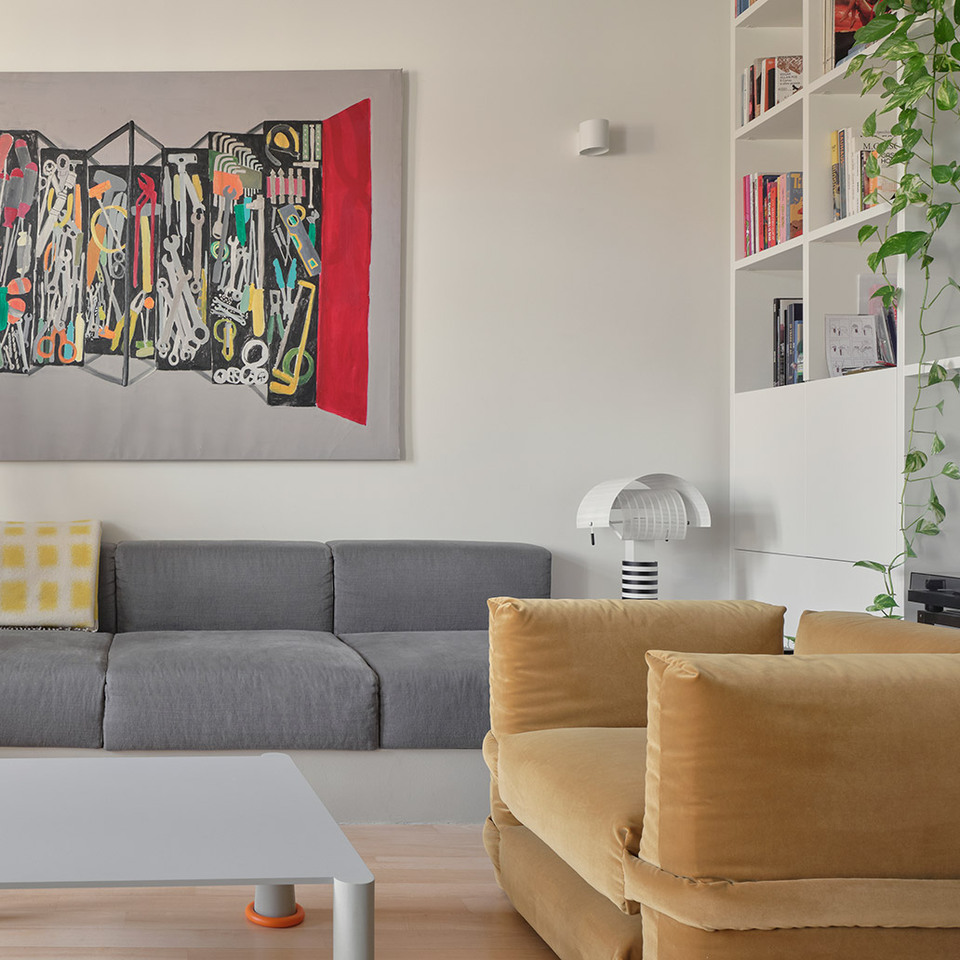 Living room with Artemide’s Ilio 10 and Shogun lamps, a grey sofa, an ochre armchair and a custom white bookshelf.