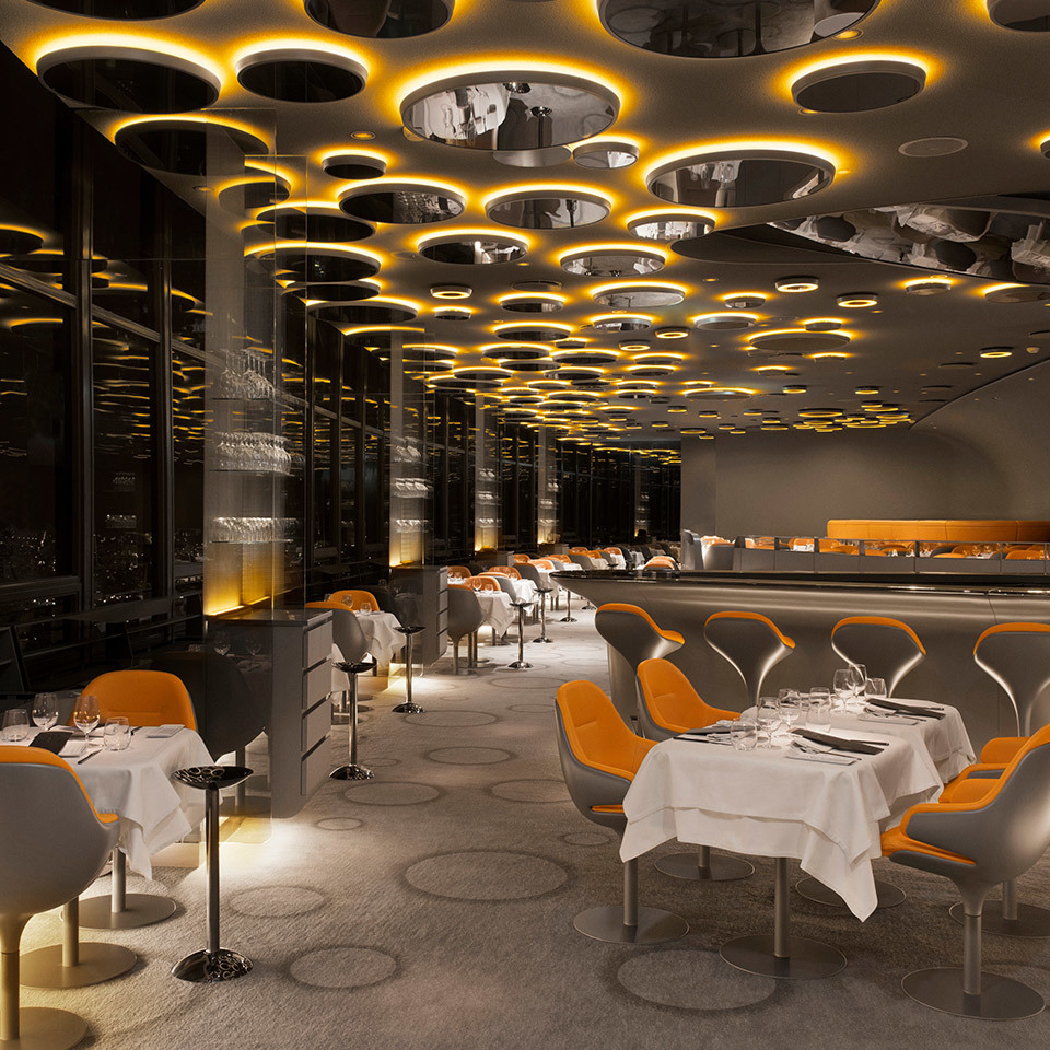 Elegant restaurant interior with circular ceiling lights emitting warm amber glow, orange modern chairs, and white-clothed dining tables.