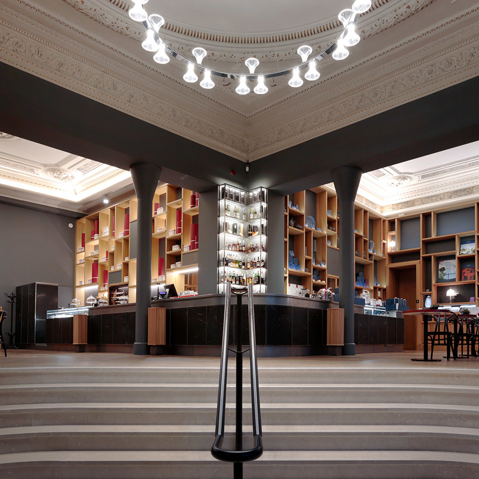 Elegant bar interior with ornate ceiling featuring Artemide pendant lights arranged in a circle above a circular counter with shelving.