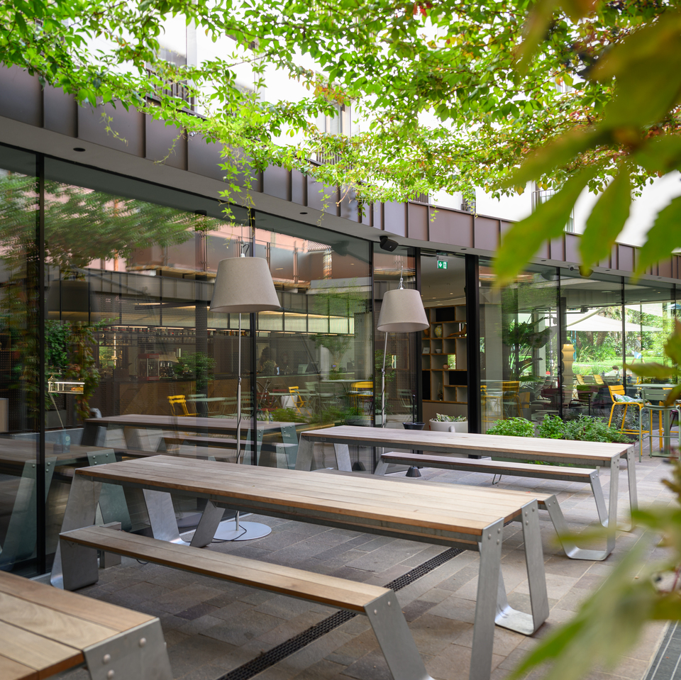 Image of the hotel exterior with tables and benches illuminated by Tolomeo Paralume Outdoor.