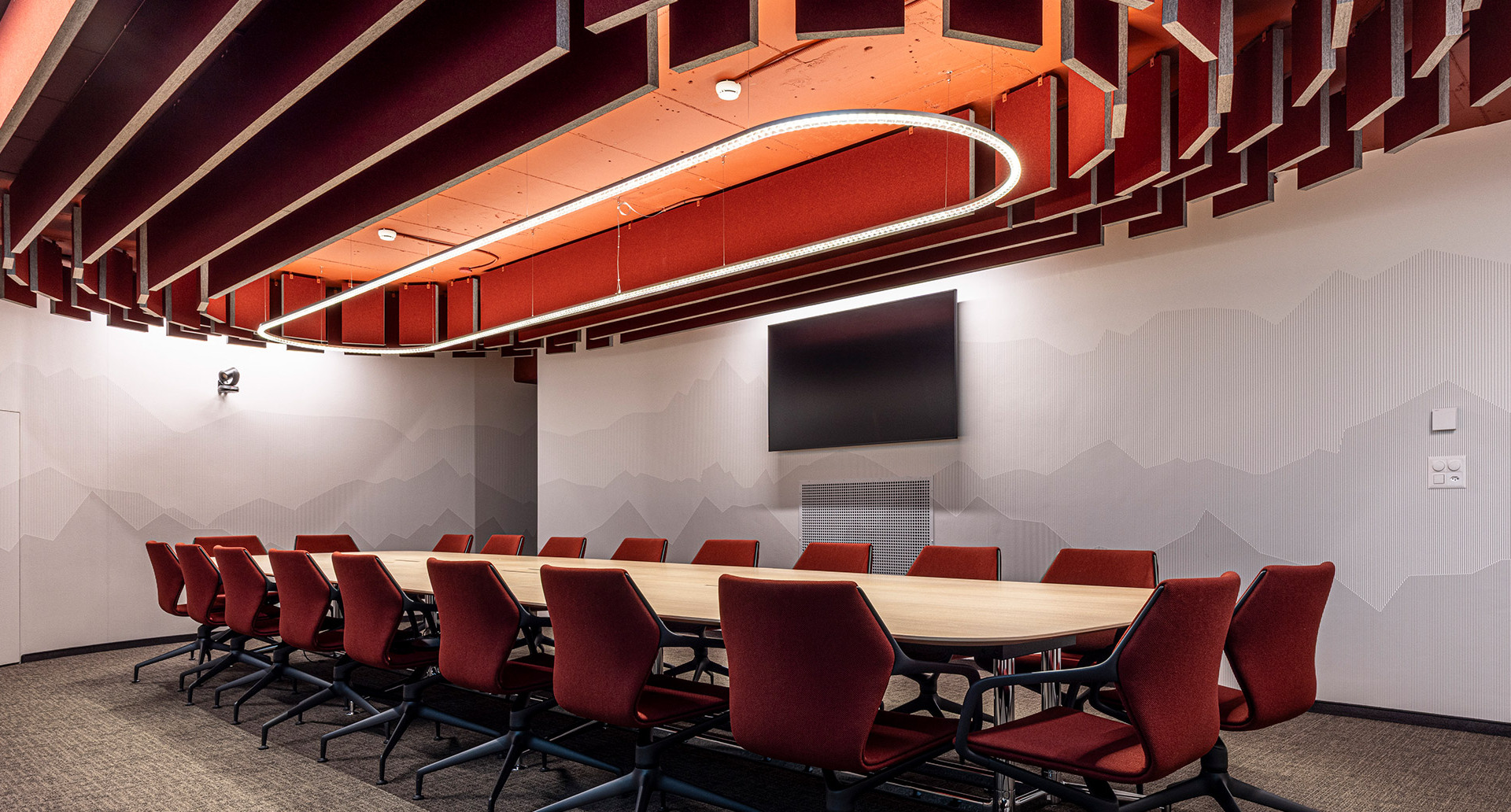 Suspended Somnĭum System light fixture above the table in a meeting room with acoustic ceiling panels.