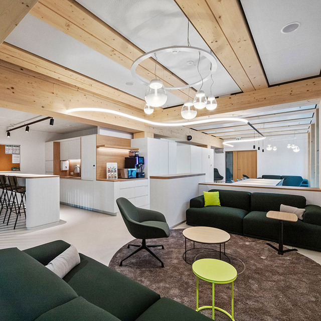 Corporate lounge with wooden beams, green sofas and suspended lighting systems above the seating areas.