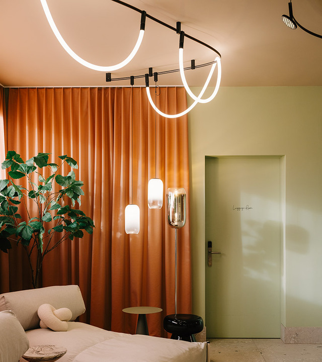 Lounge with orange curtains, light green walls, a light sofa, Gople Floor lamps in the background, and the Sylt ceiling system.