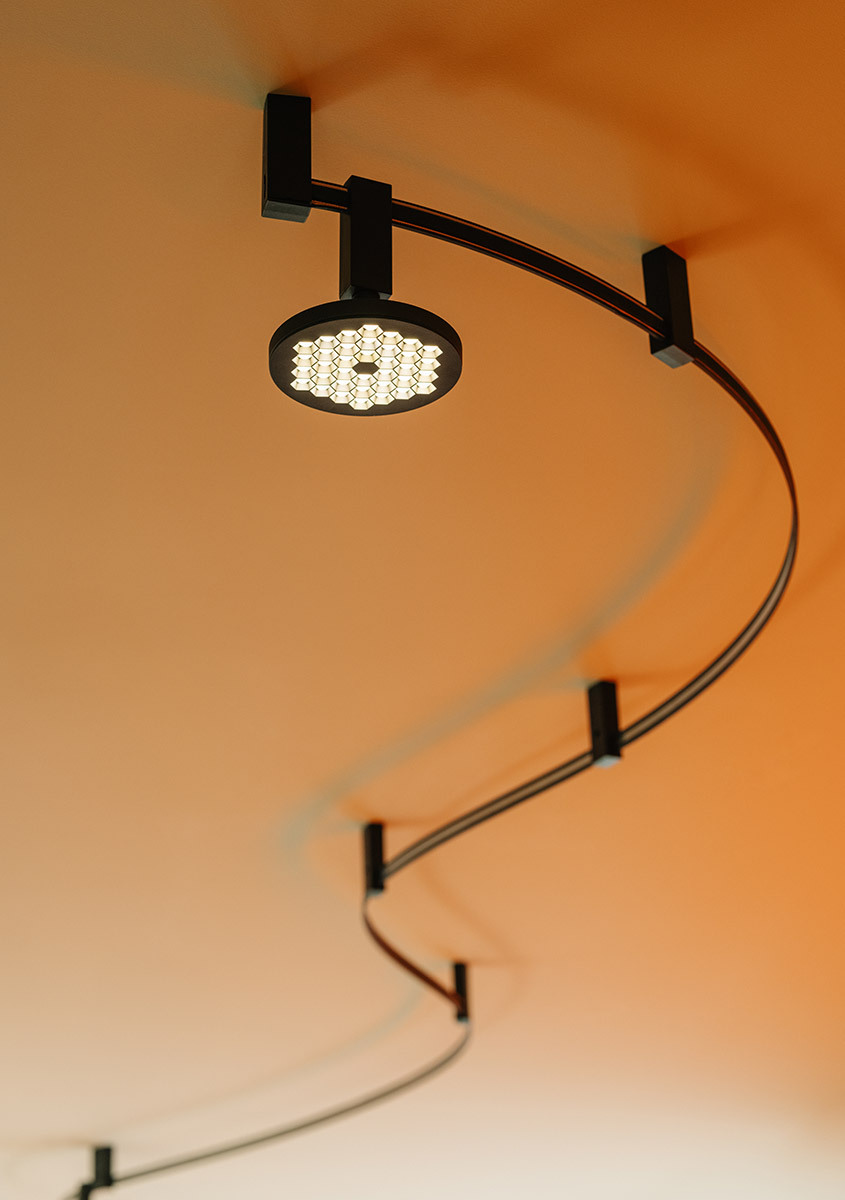 Detail of the Sylt system with a curved black track and a lit Helgoland fixture on an orange ceiling.