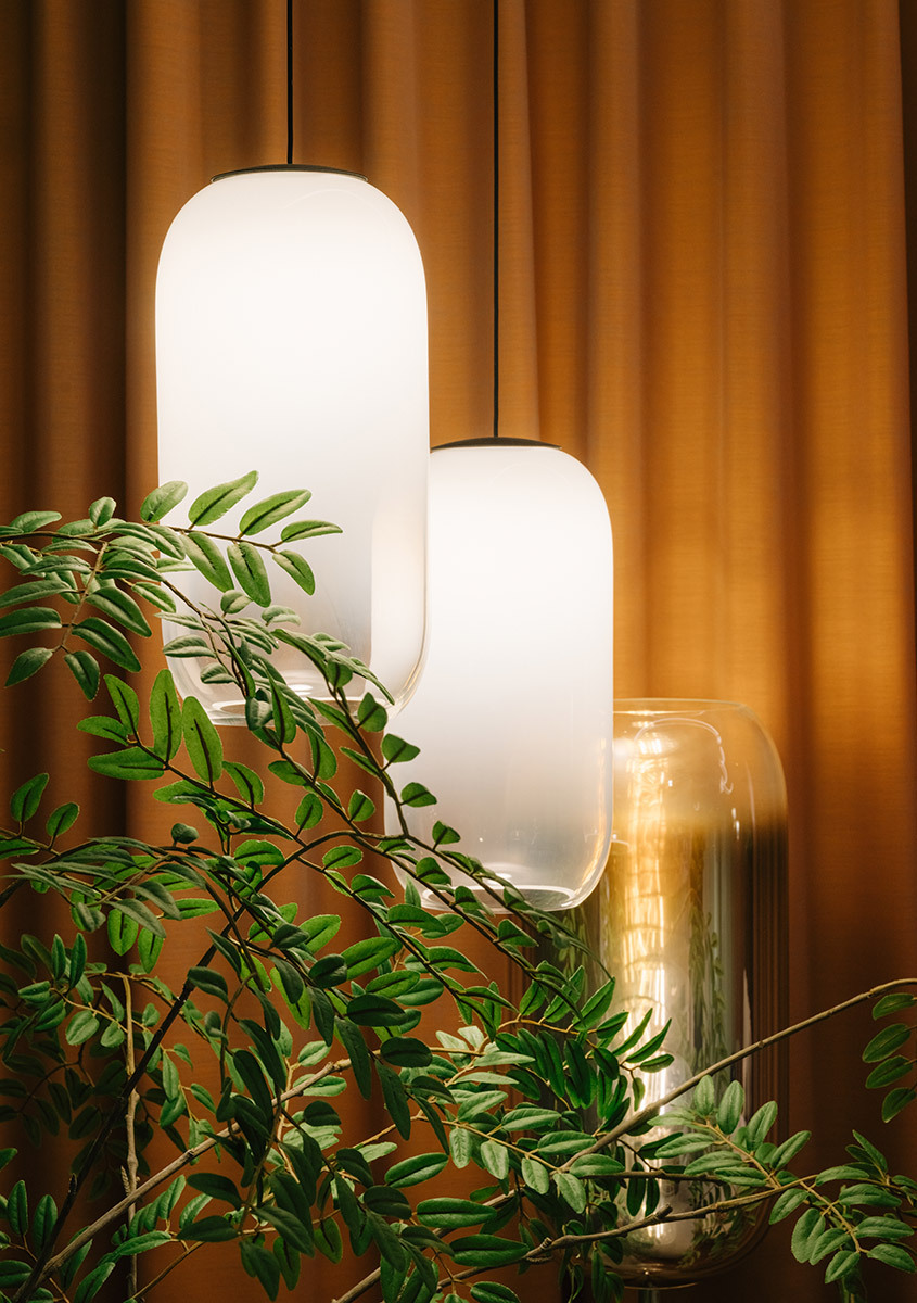 Gople pendant lamps in front of orange curtains, with decorative plants in the foreground.