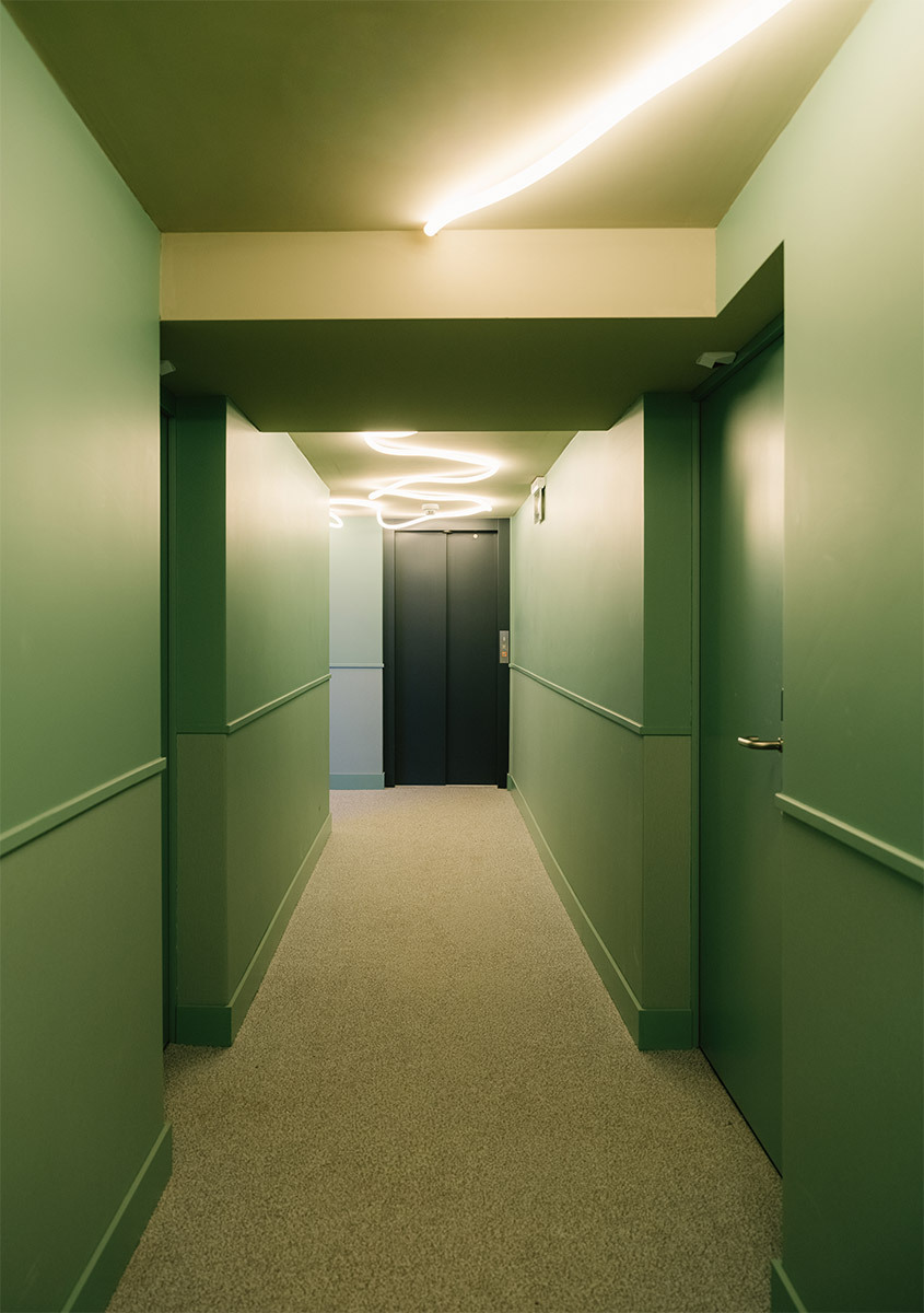 Green corridor with La Linea on the ceiling and dark doors in the background.