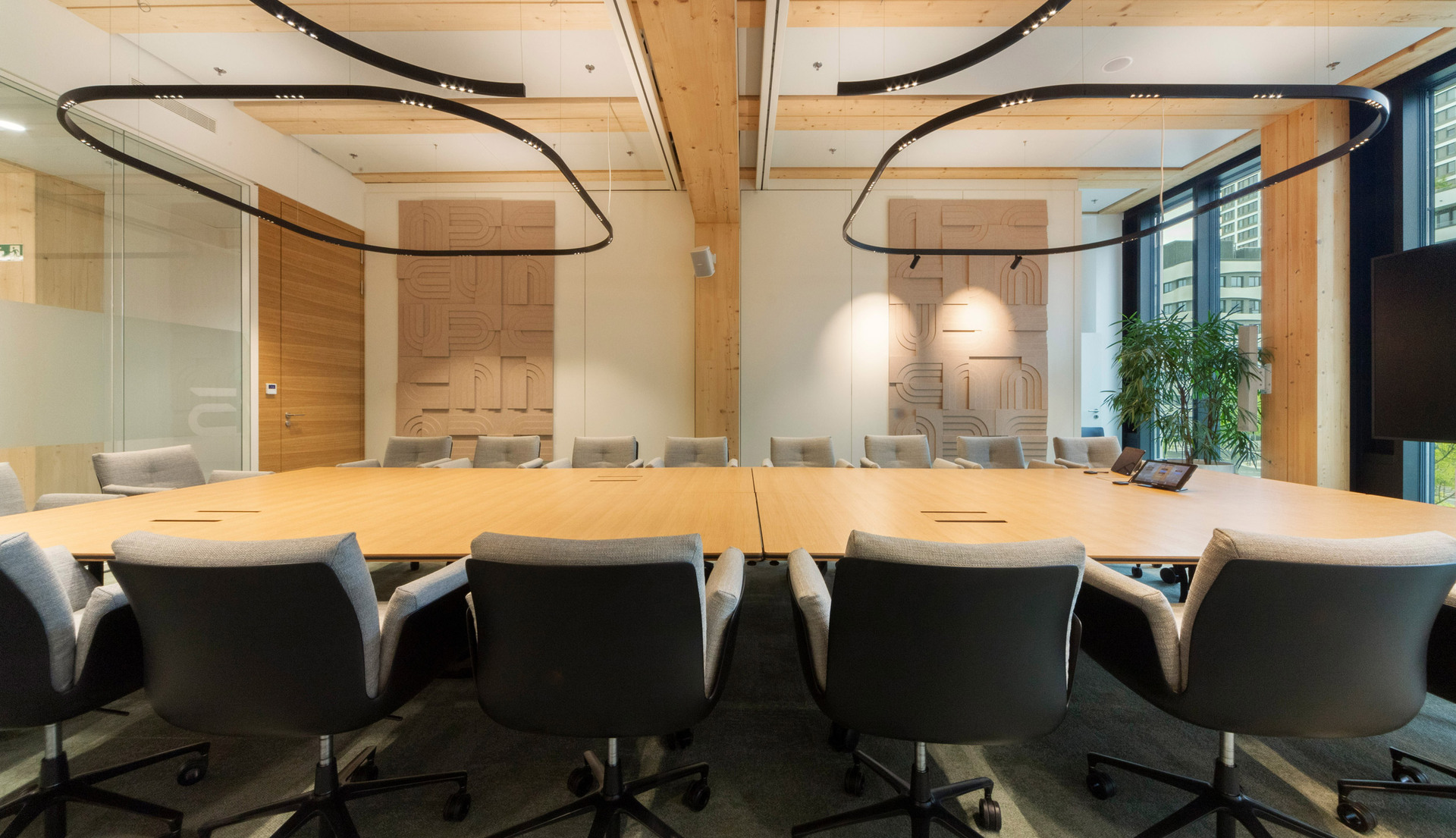 Meeting room with a large central table and a black curved lighting system suspended from the ceiling.