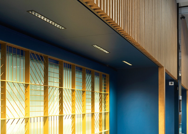 Recessed linear LED lights installed in a dark ceiling above decorative golden window grilles and blue walls with wooden slat panels