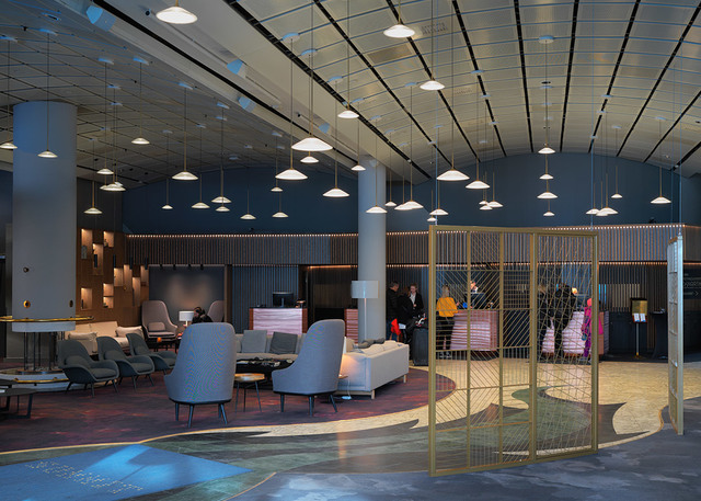 Hotel lobby with multiple white conical pendant lights hanging from a dark ceiling over a modern lounge seating area and reception desk.