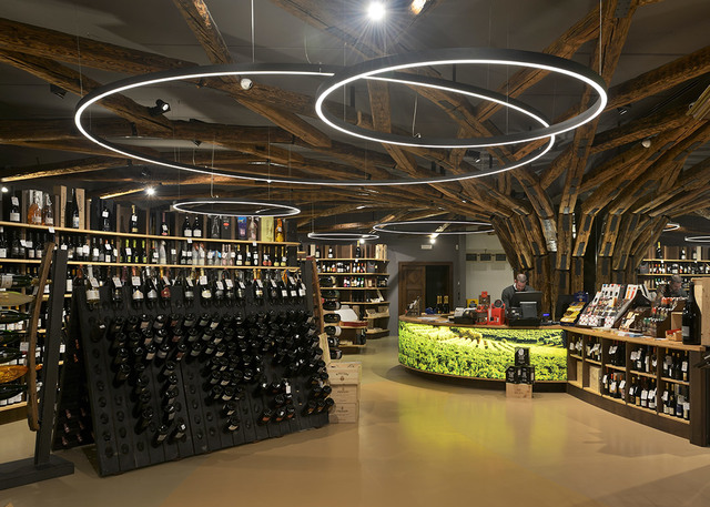 Wine shop interior with Artemide Halo circular LED pendant lights suspended from rustic wooden beam ceiling above bottle displays.