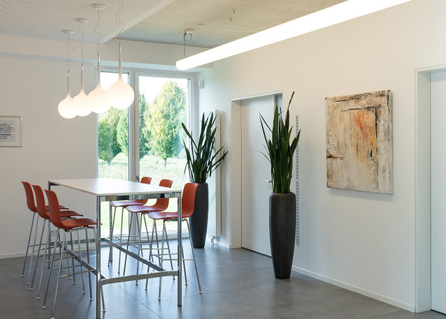 Modern dining area with white high table, red chairs, and three white globe pendant lights hanging from ceiling near large windows