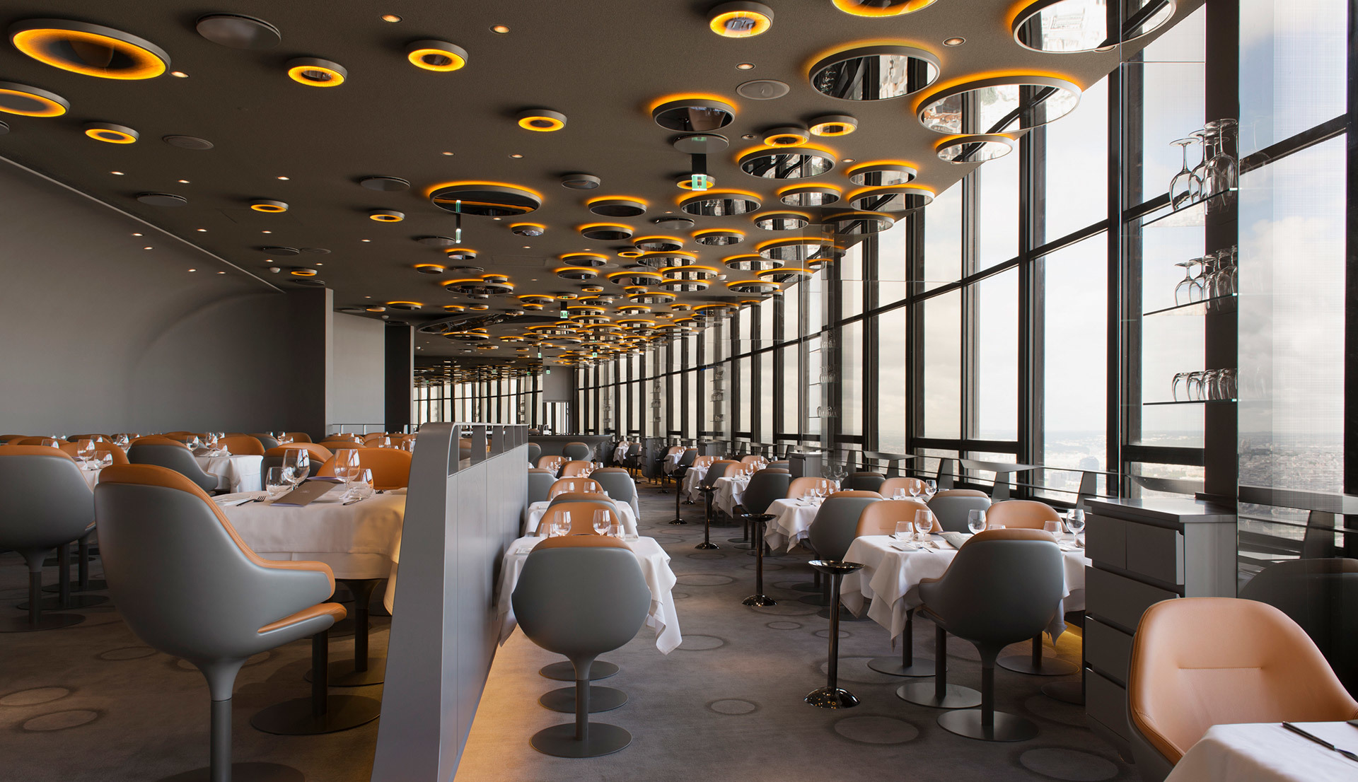 Elegant restaurant ceiling with multiple Artemide circular pendant lights in gold and black, illuminating a modern dining room with floor-to-ceiling windows.