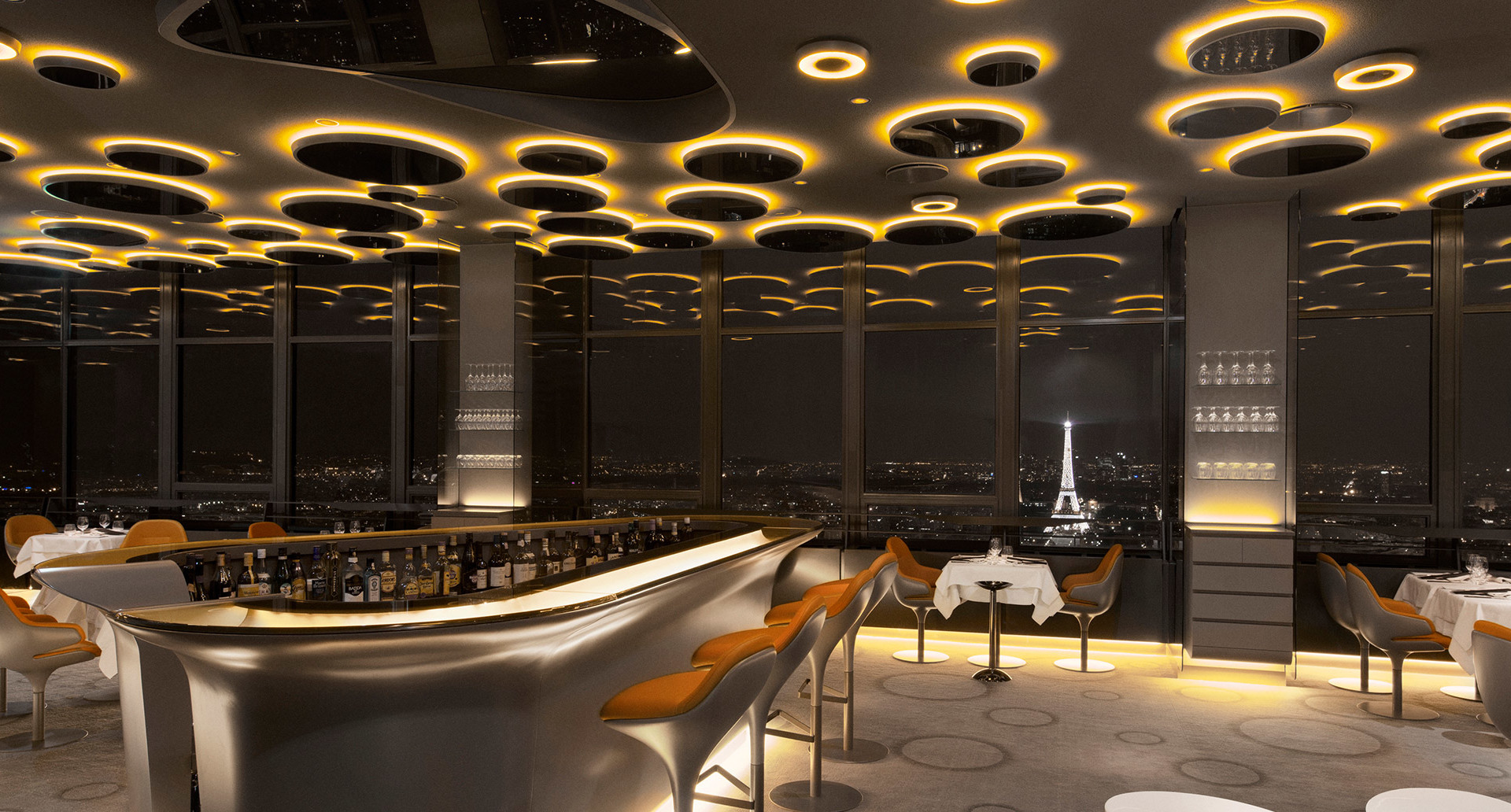 Luxury Paris restaurant with Eiffel Tower view, ceiling covered in circular Artemide LED rings emitting warm golden light
