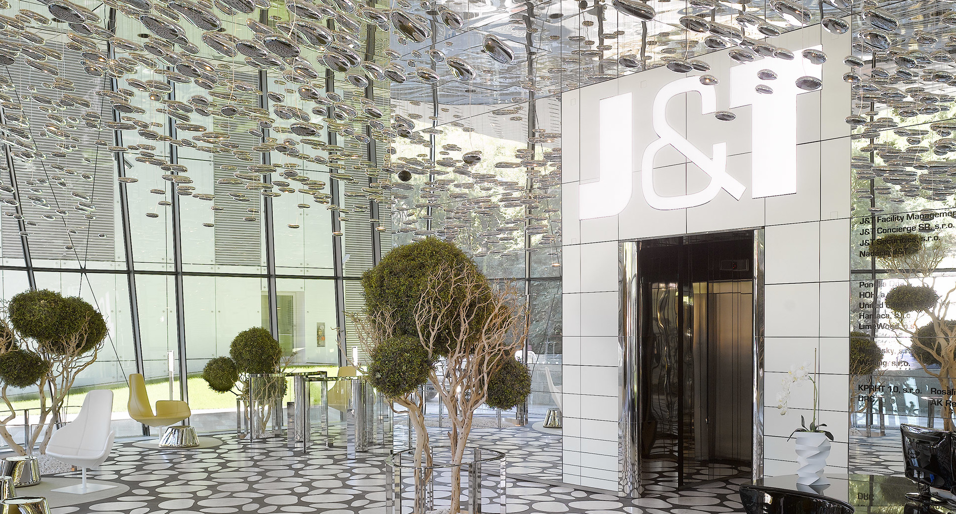 Modern lobby with mirrored ceiling featuring hundreds of small pendant lights, topiary trees, and a J&I branded entrance.