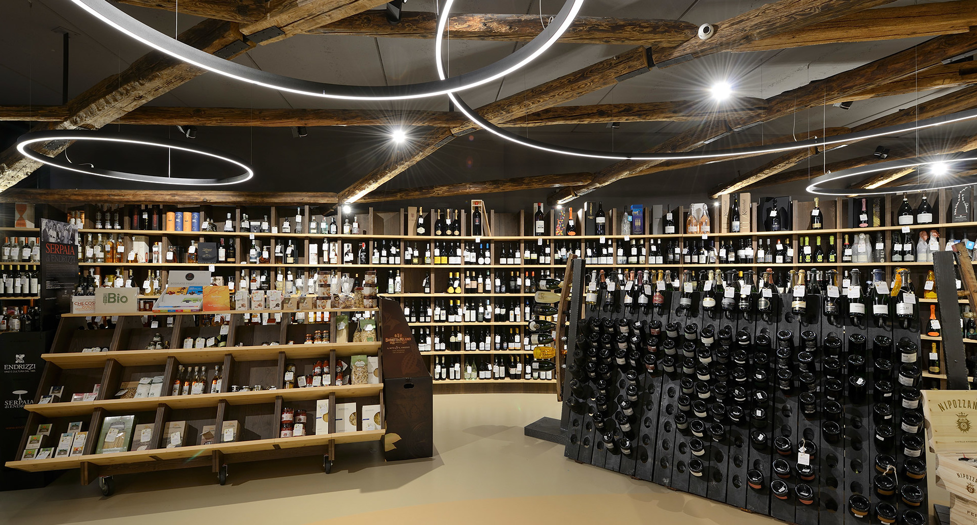 Wine shop interior with circular LED ring pendant lights illuminating wooden shelves stocked with wine bottles.