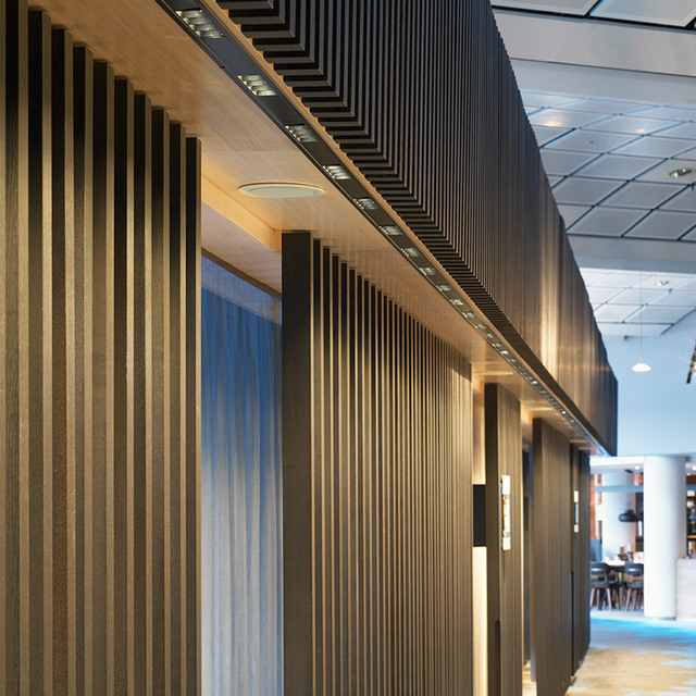 Modern corridor with dark wood slat walls, recessed LED strip lighting on ceiling, and warm wall-mounted accent lights.