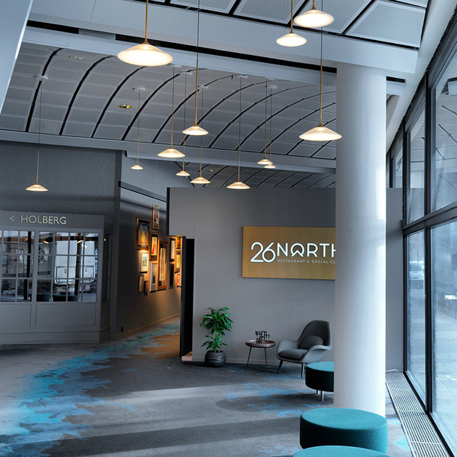 Modern lobby of 26North restaurant with multiple pendant lamps featuring flat disc shades on brass rods, illuminating a stylish reception area.
