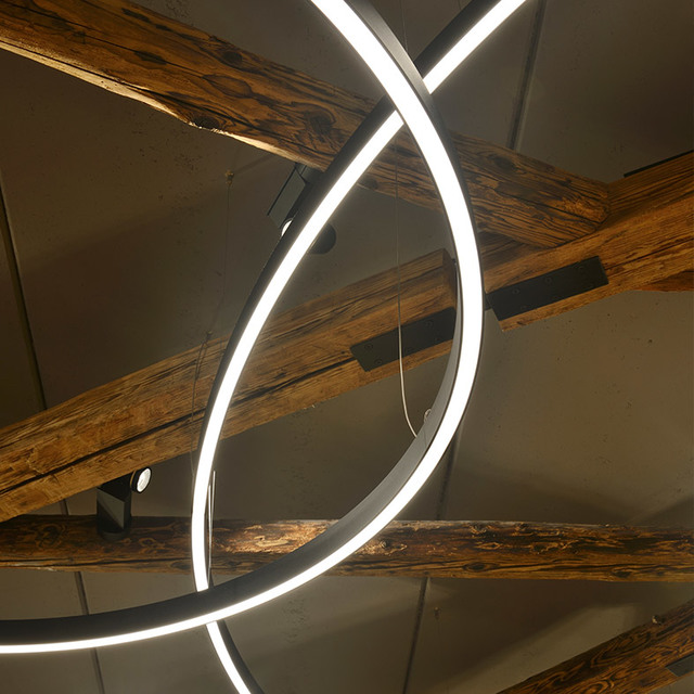 Artemide circular LED ring pendant light in black, emitting bright white light, installed among rustic wooden ceiling beams