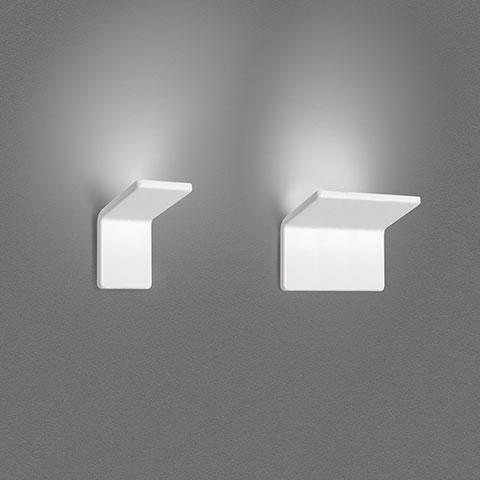 Two Artemide Cuma white wall lights with angular bracket design, casting upward light against a grey wall