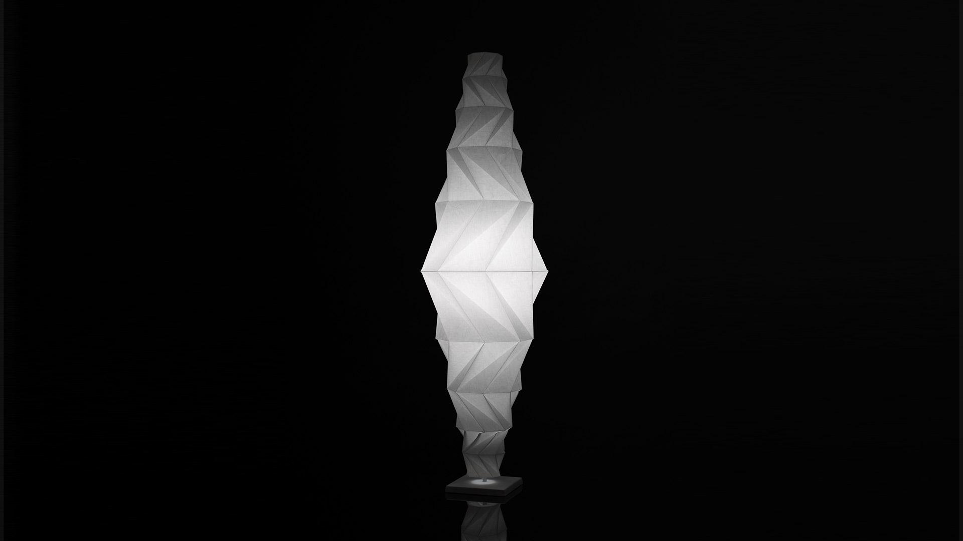 Artemide In-Ei Issey Miyake Minomushi floor lamp: tall origami-inspired white diffuser with geometric folded pattern, glowing against dark background