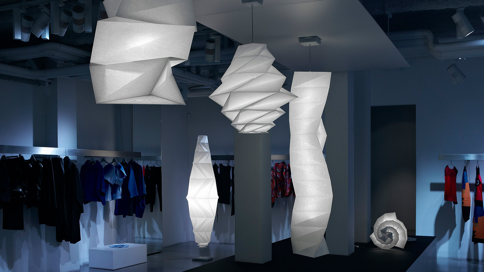 Fashion exhibition with mannequins wearing designer clothes, illuminated by Artemide In-Ei Issey Miyake Minomushi pendant and floor lamps